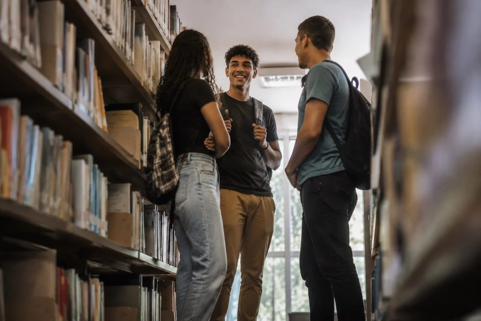 Estudantes conversando em pé entre as estantes de uma biblioteca
